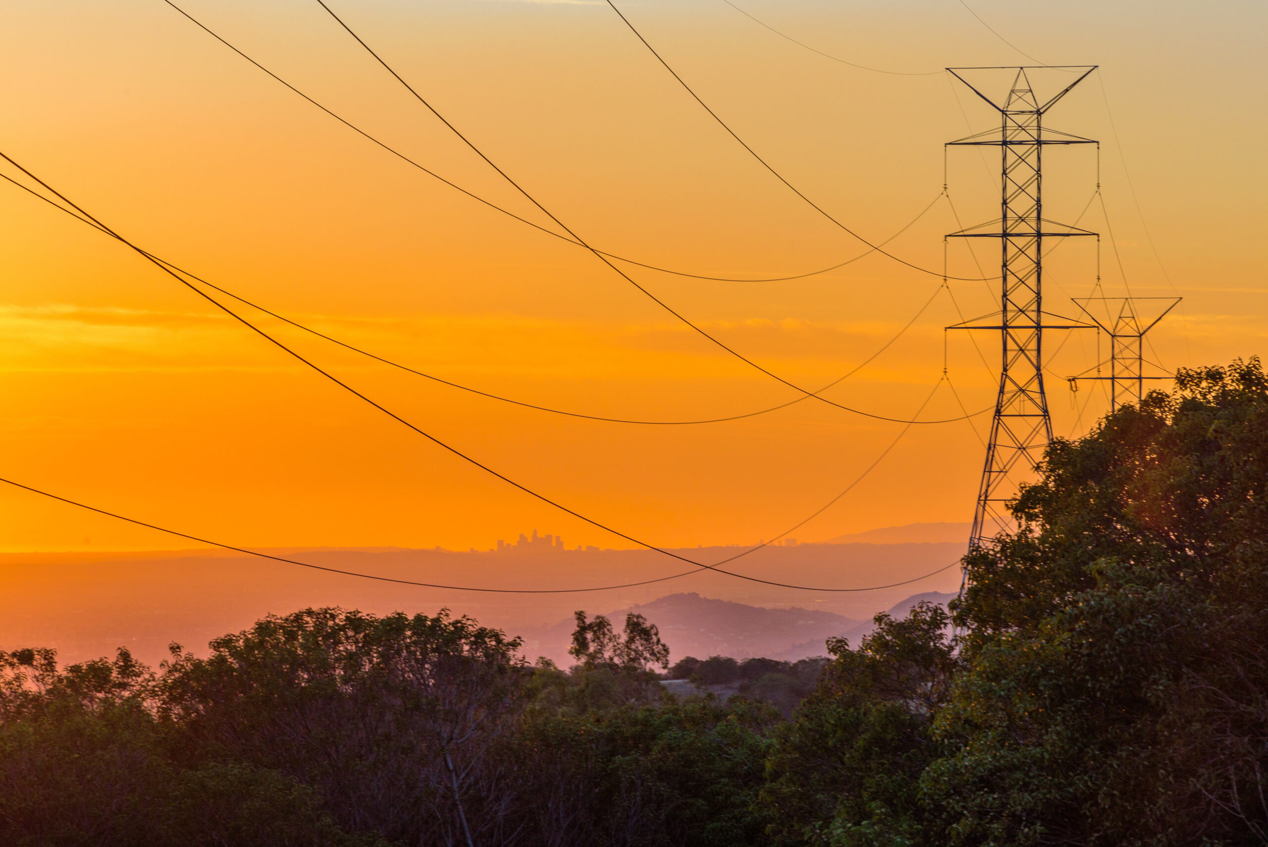 Los Angeles skyline at sunset viewed from afar through power lines.